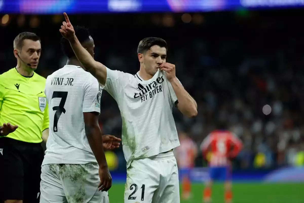 One player kisses the badge on his jersey, while another player and a referee are nearby in the field.