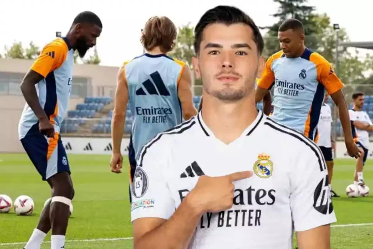 Jugadores de fútbol del Real Madrid entrenando en el campo, con uno de ellos en primer plano señalando el escudo de su camiseta.