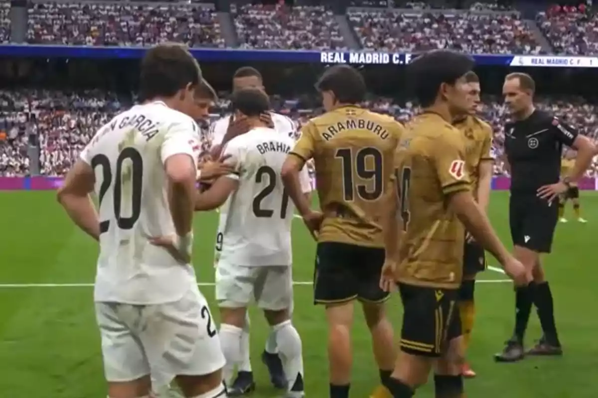 Jugadores de fútbol de dos equipos diferentes conversan en el campo durante un partido, con un árbitro observando cerca y una multitud en las gradas. Jugadores de fútbol de dos equipos diferentes conversan en el campo durante un partido, con un árbitro observando cerca y una multitud en las gradas.