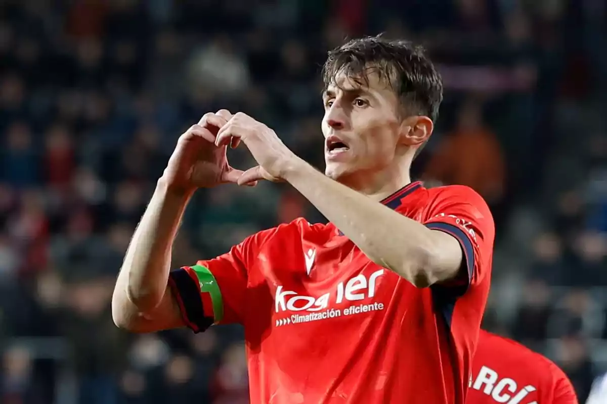 Futbolista con uniforme rojo celebrando un gol haciendo un gesto de corazón con las manos en un estadio lleno de espectadores Futbolista con uniforme rojo celebrando un gol haciendo un gesto de corazón con las manos en un estadio lleno de espectadores