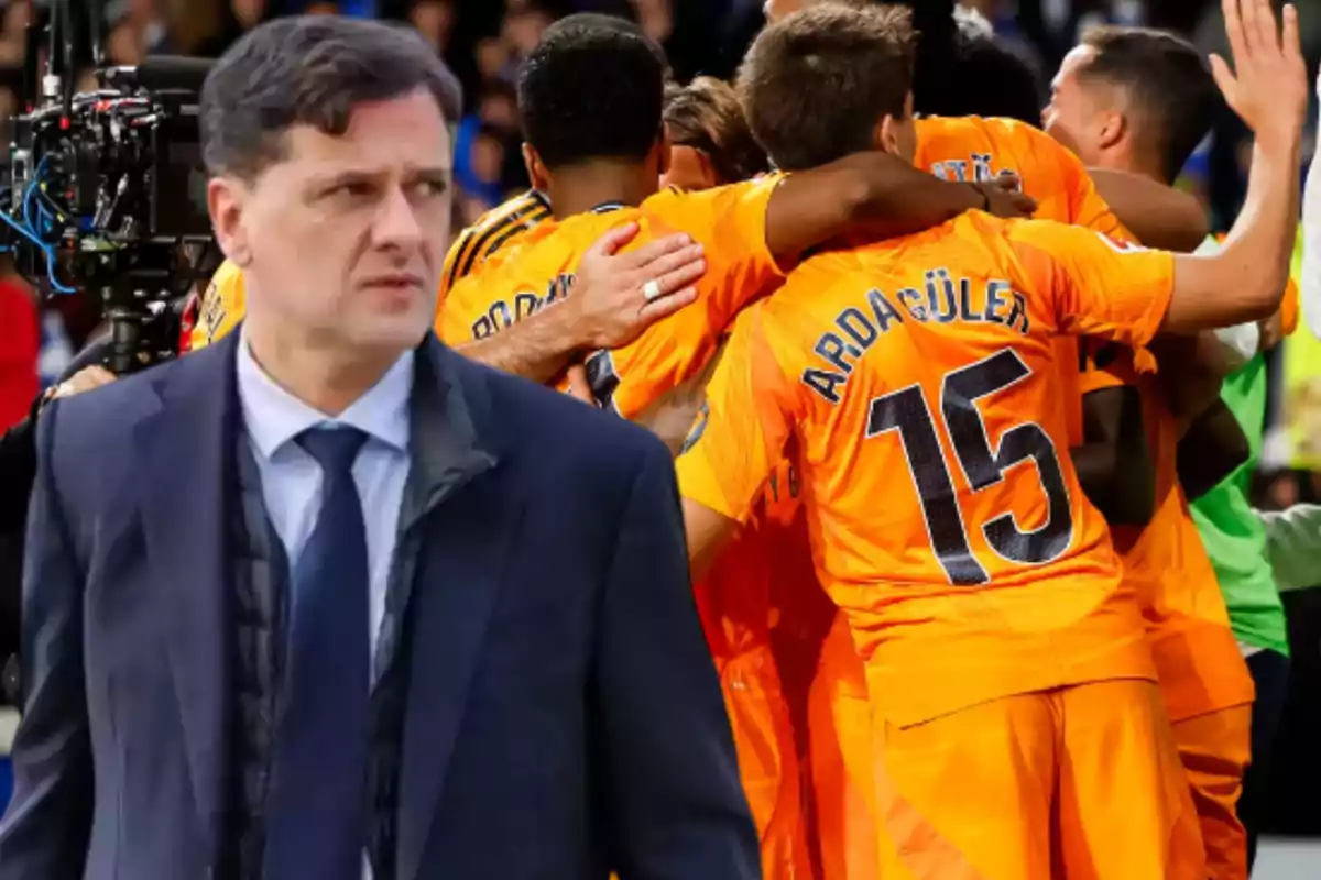 A man in a dark suit is in the foreground while a group of players in orange uniforms celebrates in the background.