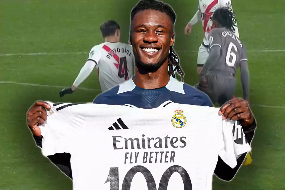 Un jugador de fútbol sonríe mientras sostiene una camiseta del Real Madrid con el número 100, en el fondo se observa un partido en progreso.