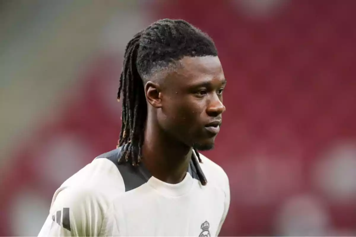 Un jugador de fútbol con camiseta blanca y peinado con trenzas en un campo de juego. Un jugador de fútbol con camiseta blanca y peinado con trenzas en un campo de juego.