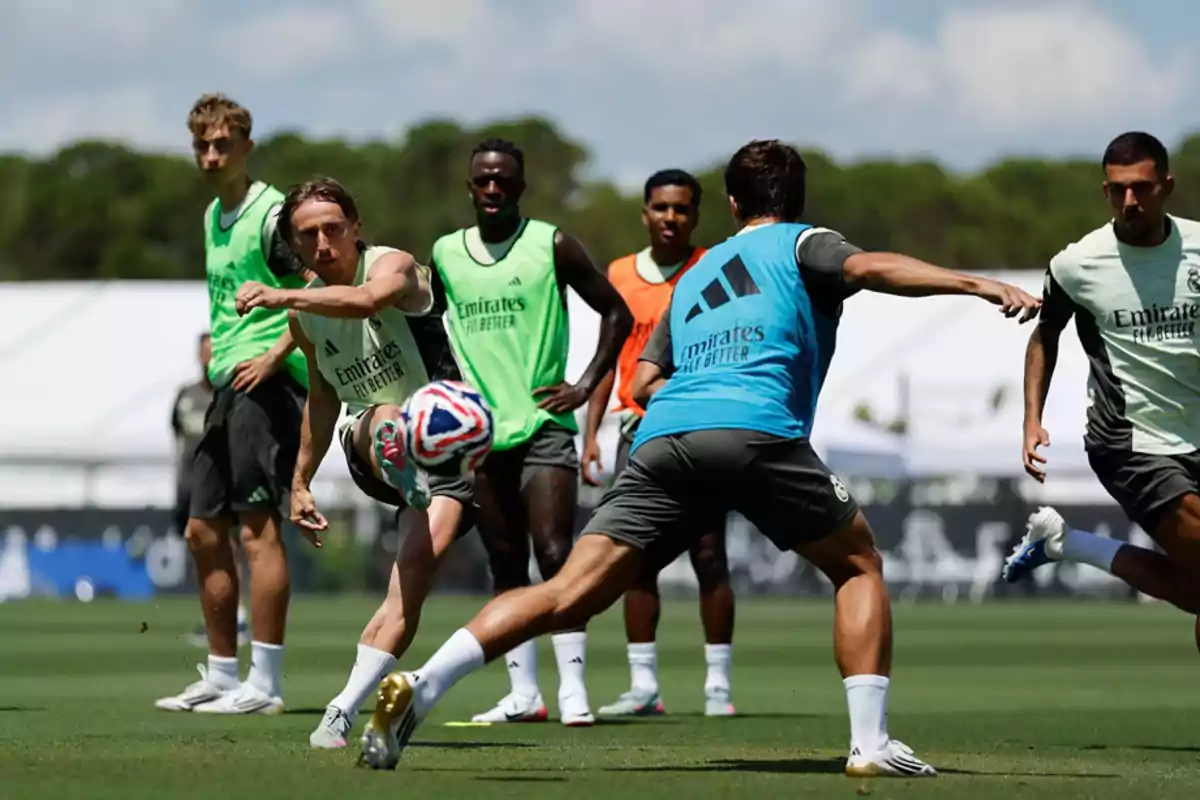 Soccer players training on a grass field while one of them kicks the ball surrounded by teammates wearing bibs of different colors. Soccer players training on a grass field while one of them kicks the ball surrounded by teammates wearing bibs of different colors.