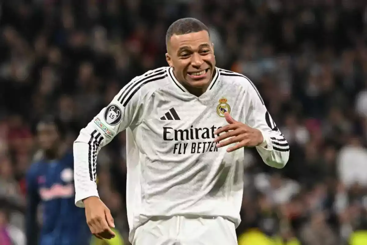 Un jugador de fútbol con uniforme blanco sonríe en el campo durante un partido.