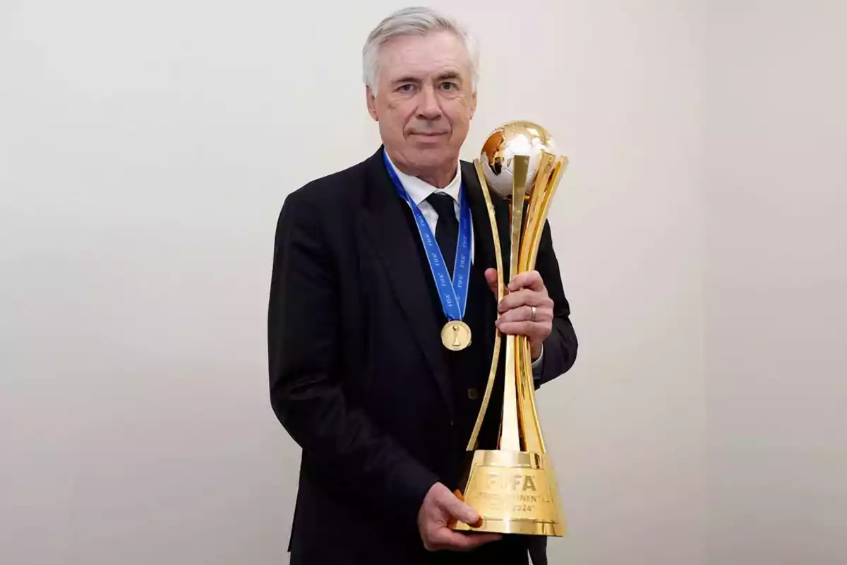 A gray-haired man in a dark suit holds a golden trophy with a medal hanging from his neck. A gray-haired man in a dark suit holds a golden trophy with a medal hanging from his neck.
