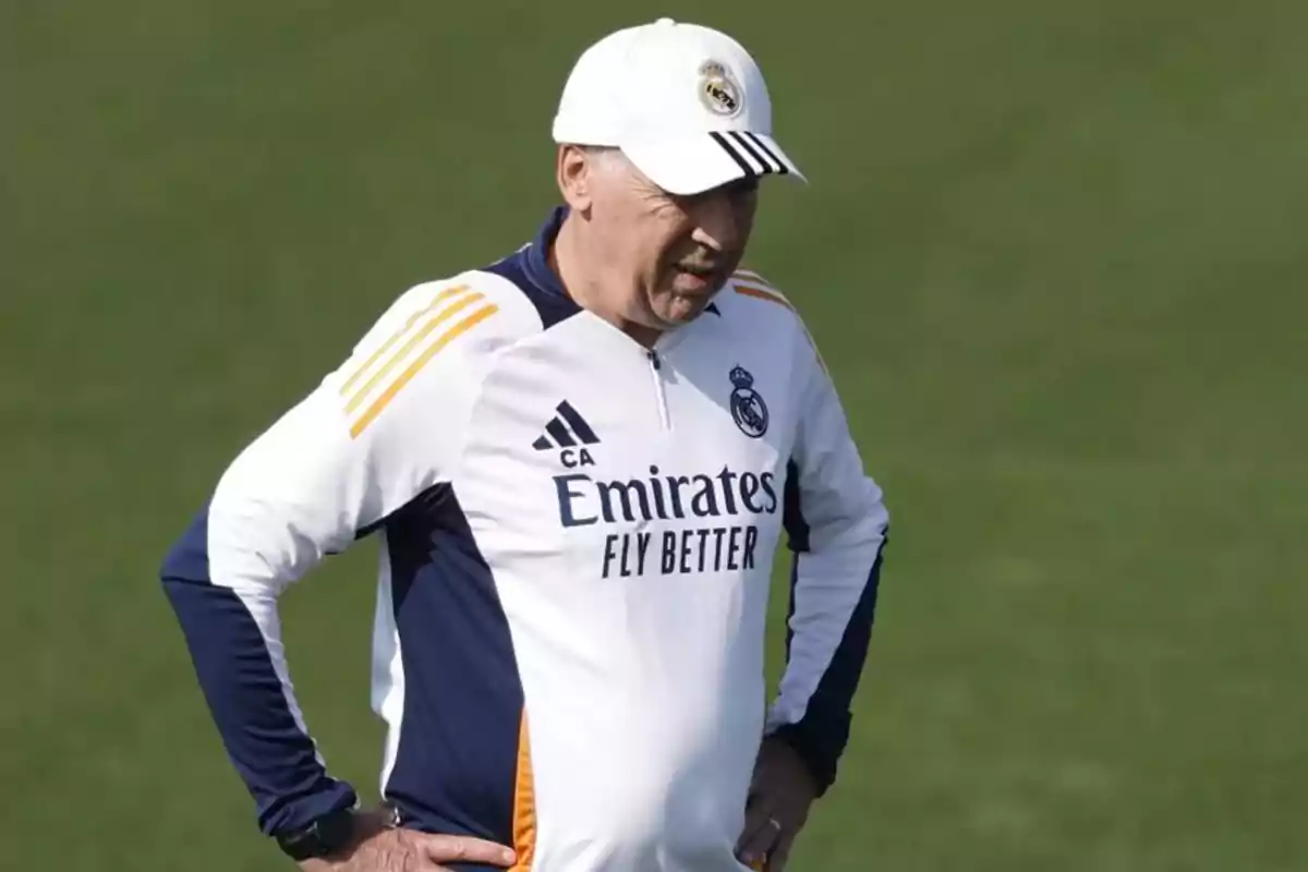 Un entrenador de fútbol con gorra y uniforme del Real Madrid en un campo de entrenamiento.