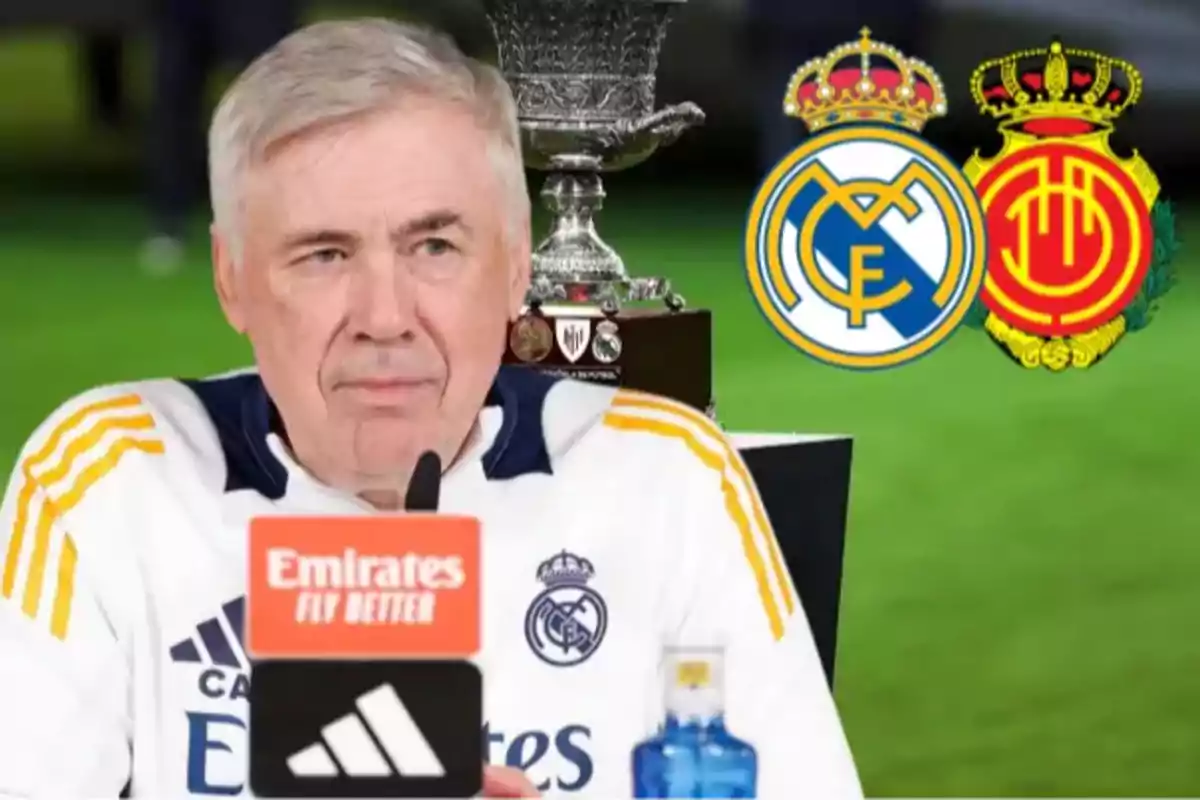 A soccer coach at a press conference with the logos of two teams and a trophy in the background.