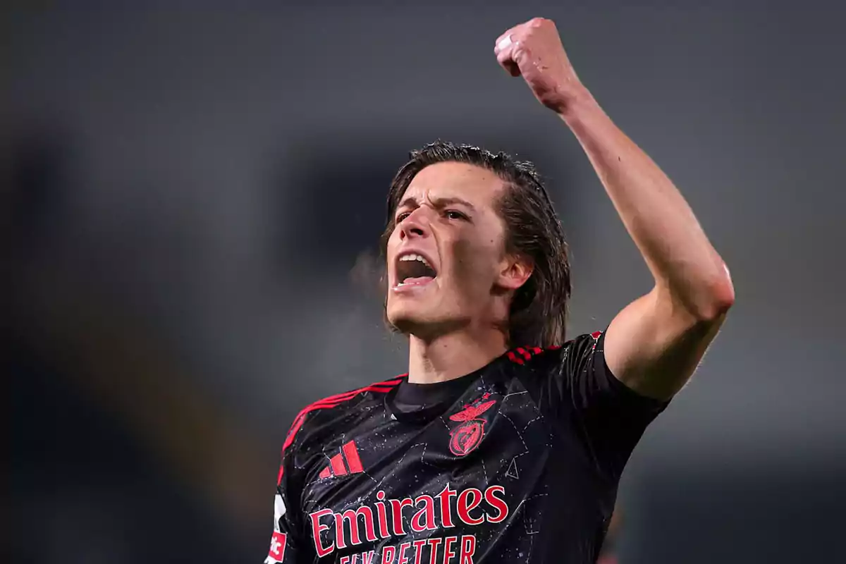 A player celebrating with a raised fist while wearing a black Benfica team jersey. A player celebrating with a raised fist while wearing a black Benfica team jersey.