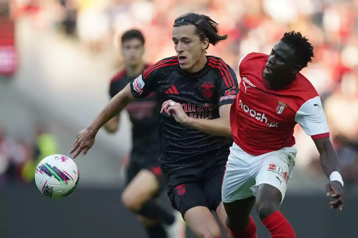 Two players compete for the ball during a match, one wearing a black uniform and the other wearing a red and white uniform. Two players compete for the ball during a match, one wearing a black uniform and the other wearing a red and white uniform.