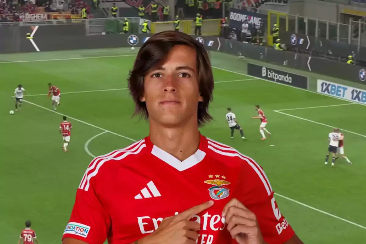 A player wearing a Benfica jersey points to the team's crest while a match unfolds in the background.
