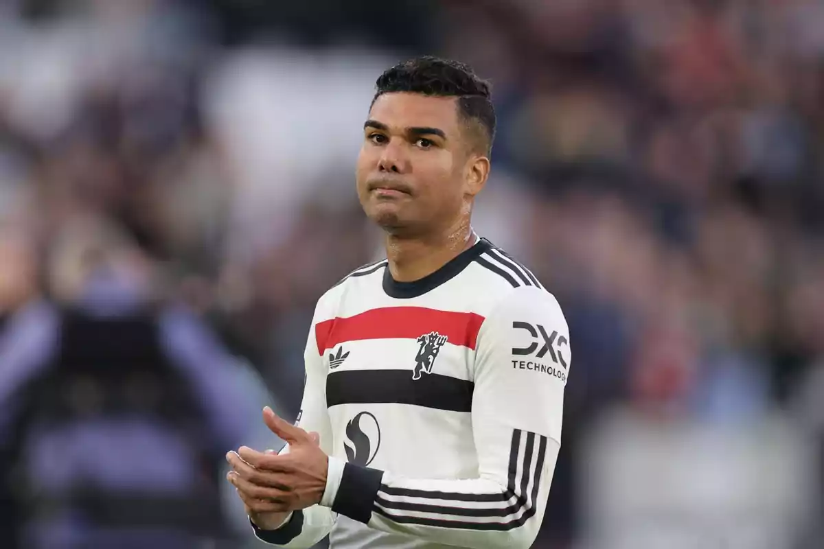 Un jugador de fútbol con uniforme blanco y negro aplaude en el campo.