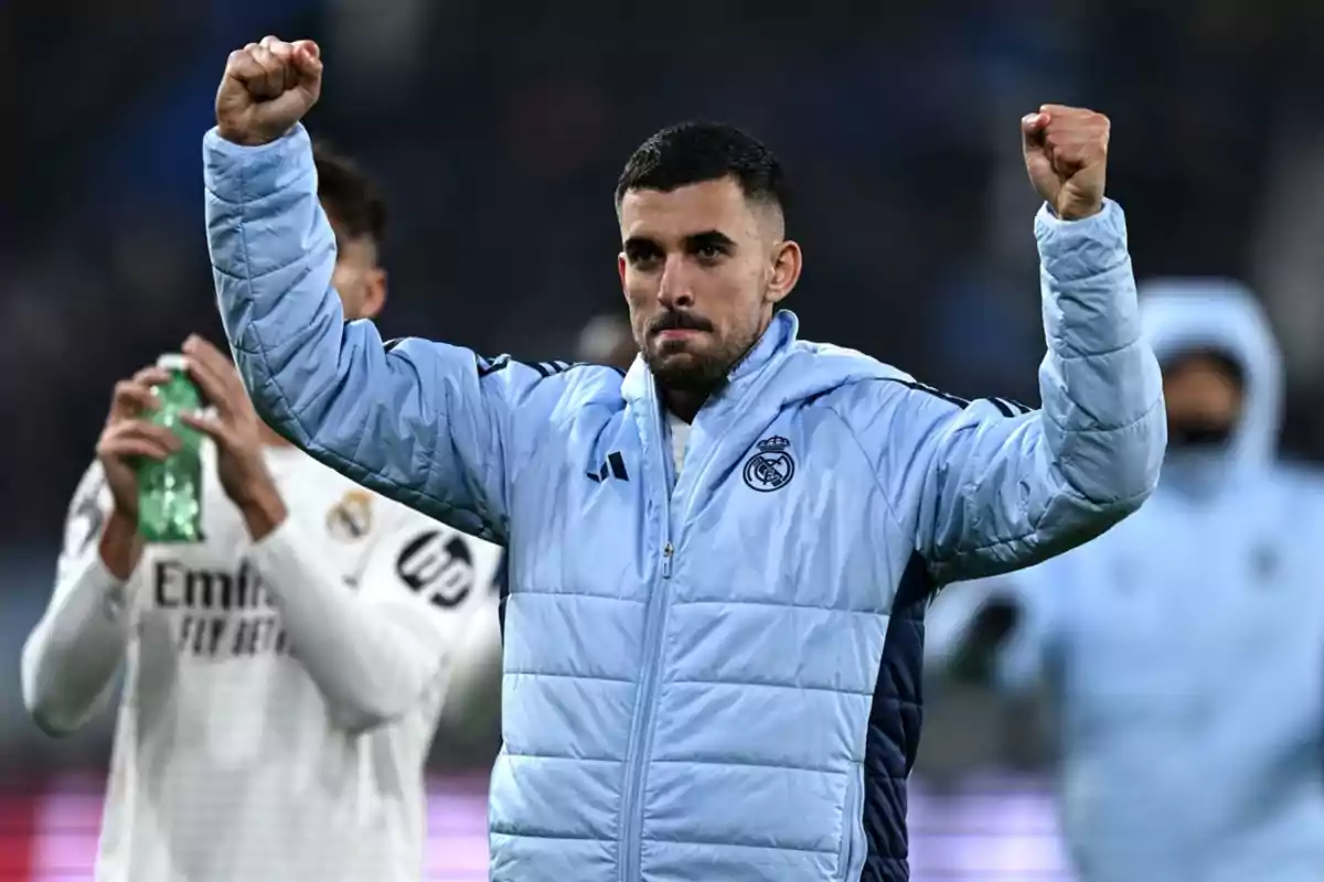 A soccer player in a blue jacket raises his arms in victory on the field. A soccer player in a blue jacket raises his arms in victory on the field.