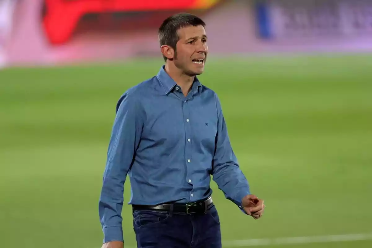 Man standing on a soccer field wearing a blue jersey and dark pants while gesturing with his hand Man standing on a soccer field wearing a blue jersey and dark pants while gesturing with his hand