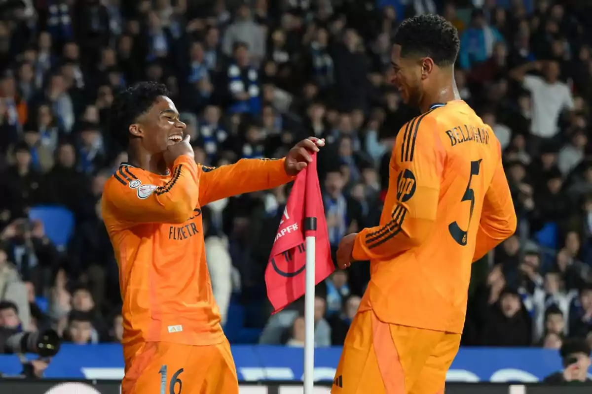 Two players in orange uniforms celebrate next to a flag on the field.