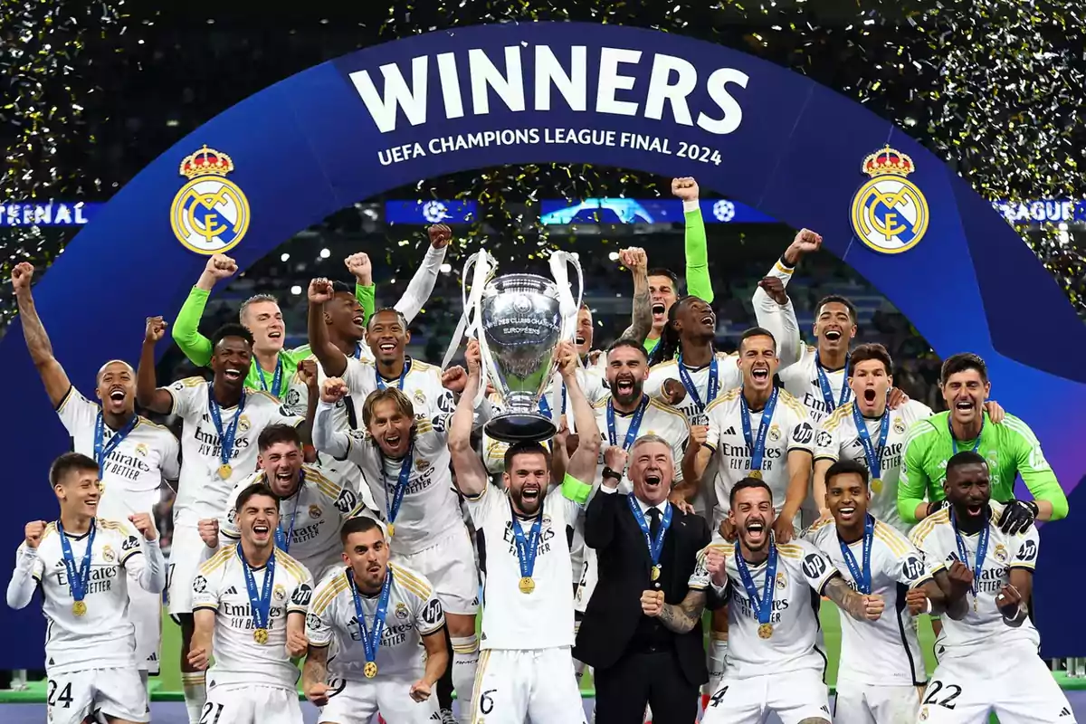 Players of a soccer team celebrate with the UEFA Champions League 2024 trophy under an arch reading "Winners" as golden confetti falls around them.