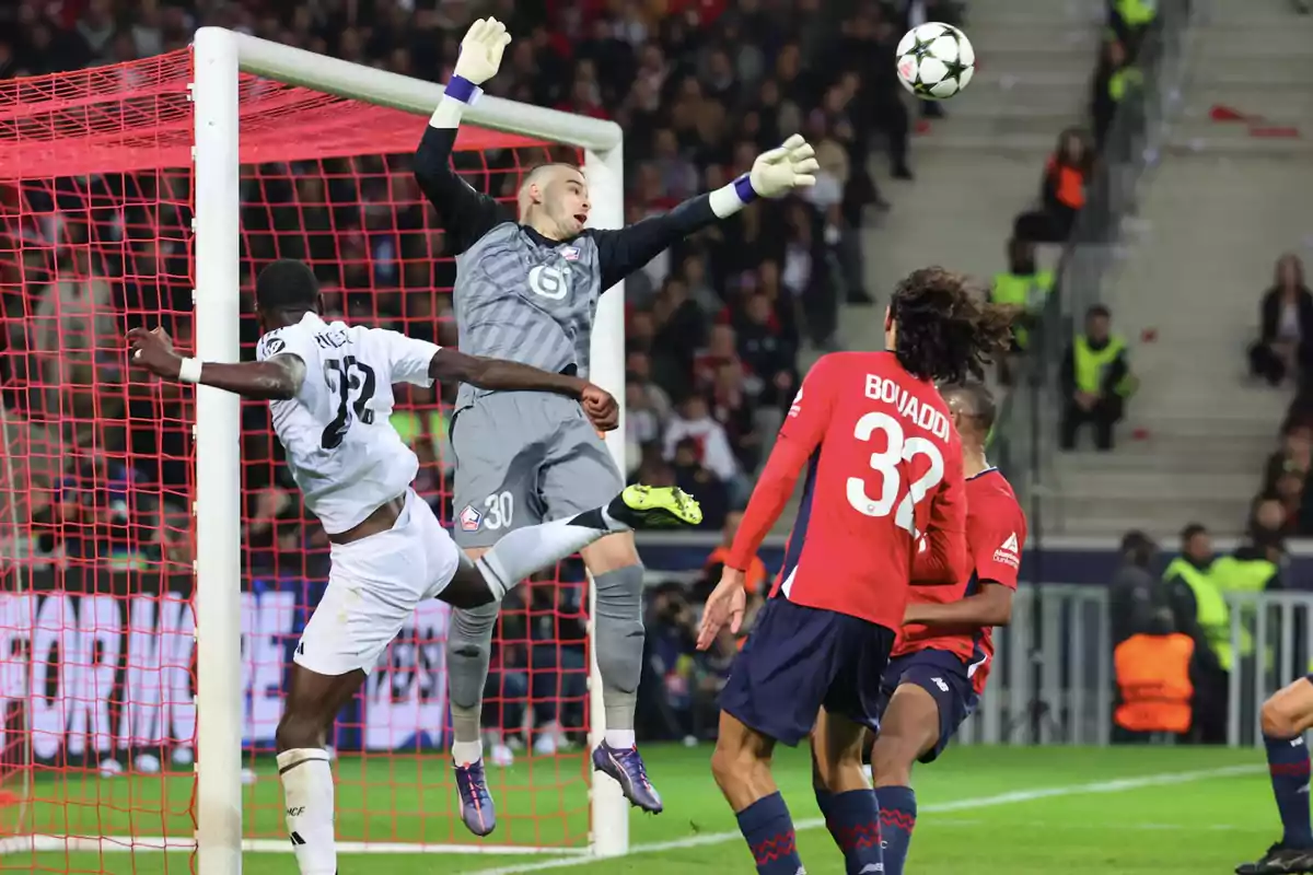 Goalkeeper jumping to try to stop a ball during a soccer match while an opposing player heads the ball near the goal and other players watch the play. Goalkeeper jumping to try to stop a ball during a soccer match while an opposing player heads the ball near the goal and other players watch the play.