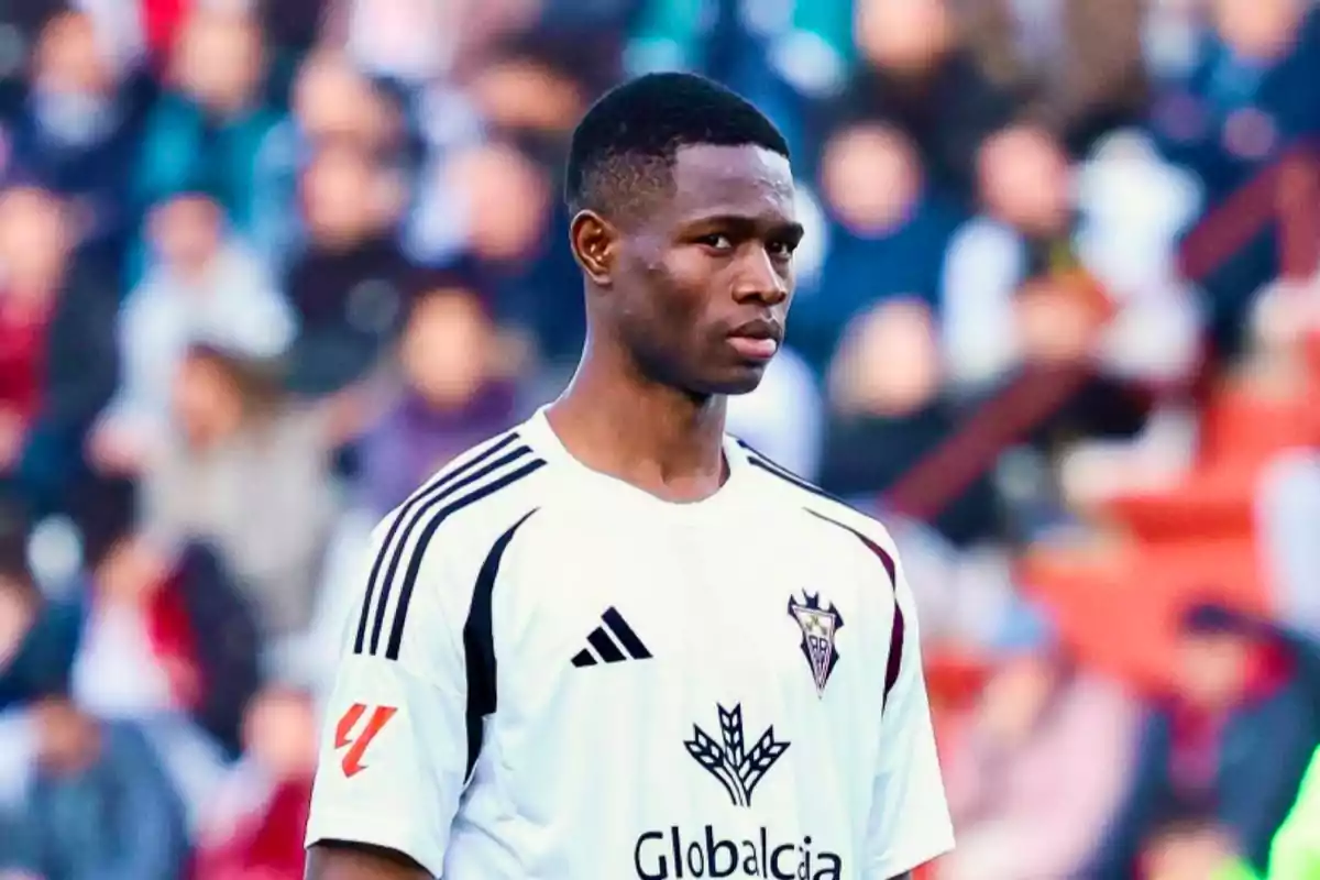 Soccer player in a white uniform with black details in a stadium full of blurred spectators Soccer player in a white uniform with black details in a stadium full of blurred spectators