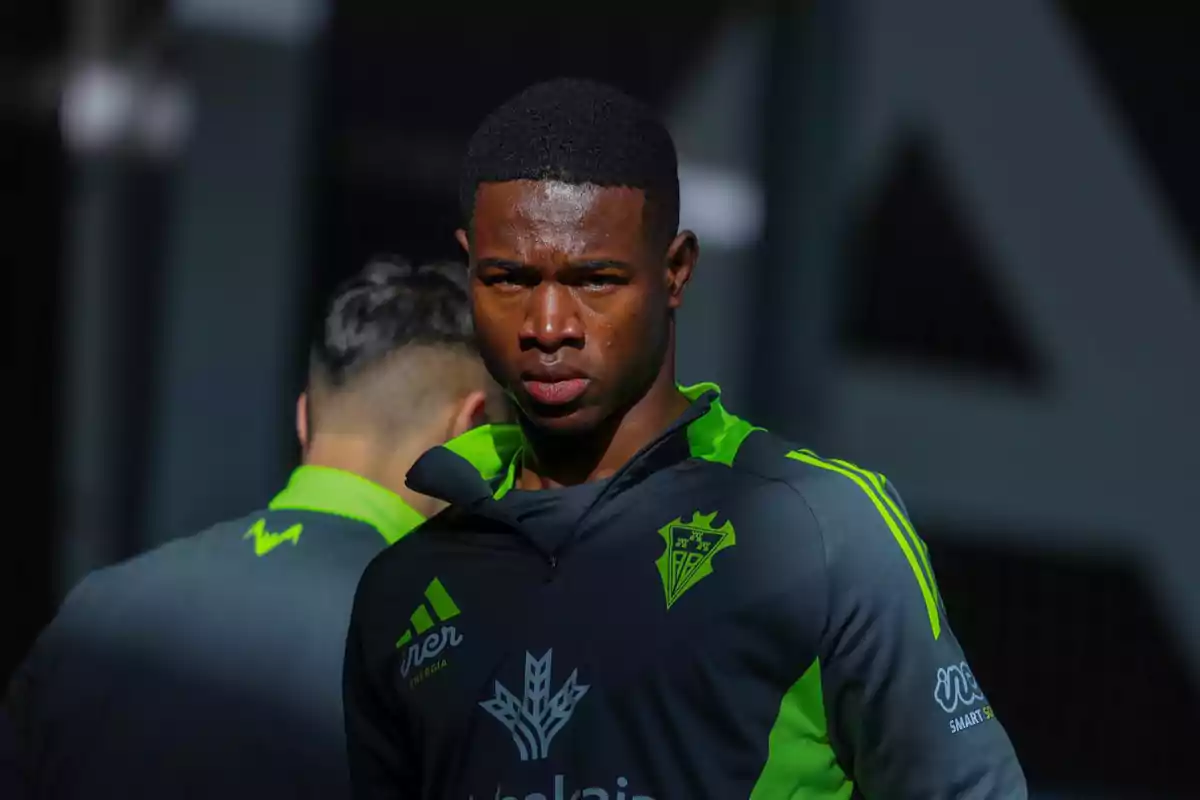 Soccer player in a gray and green Real Betis uniform in the foreground looking at the camera Soccer player in a gray and green Real Betis uniform in the foreground looking at the camera