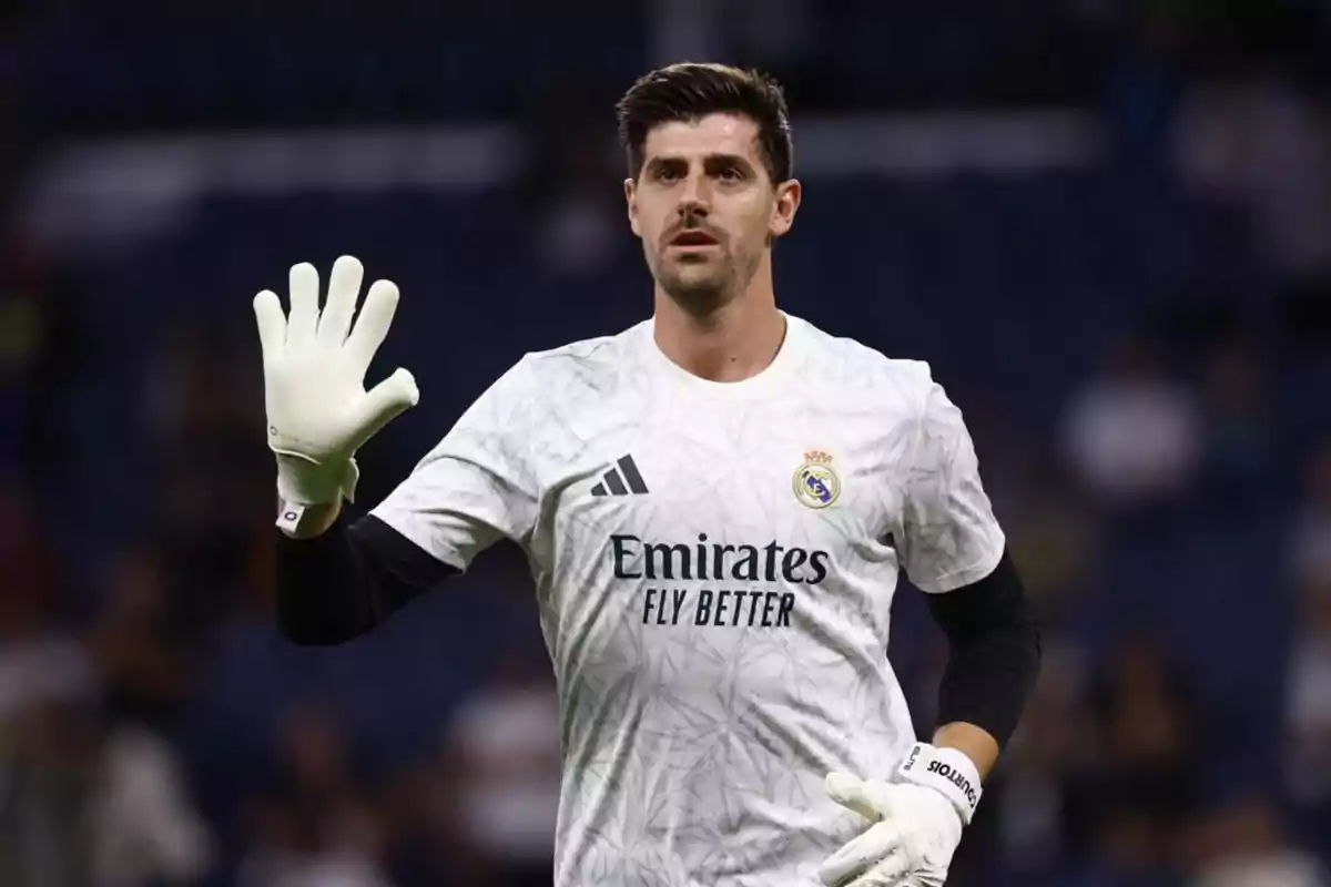 A soccer goalkeeper in a white uniform and gloves raising one hand in a stadium. A soccer goalkeeper in a white uniform and gloves raising one hand in a stadium.