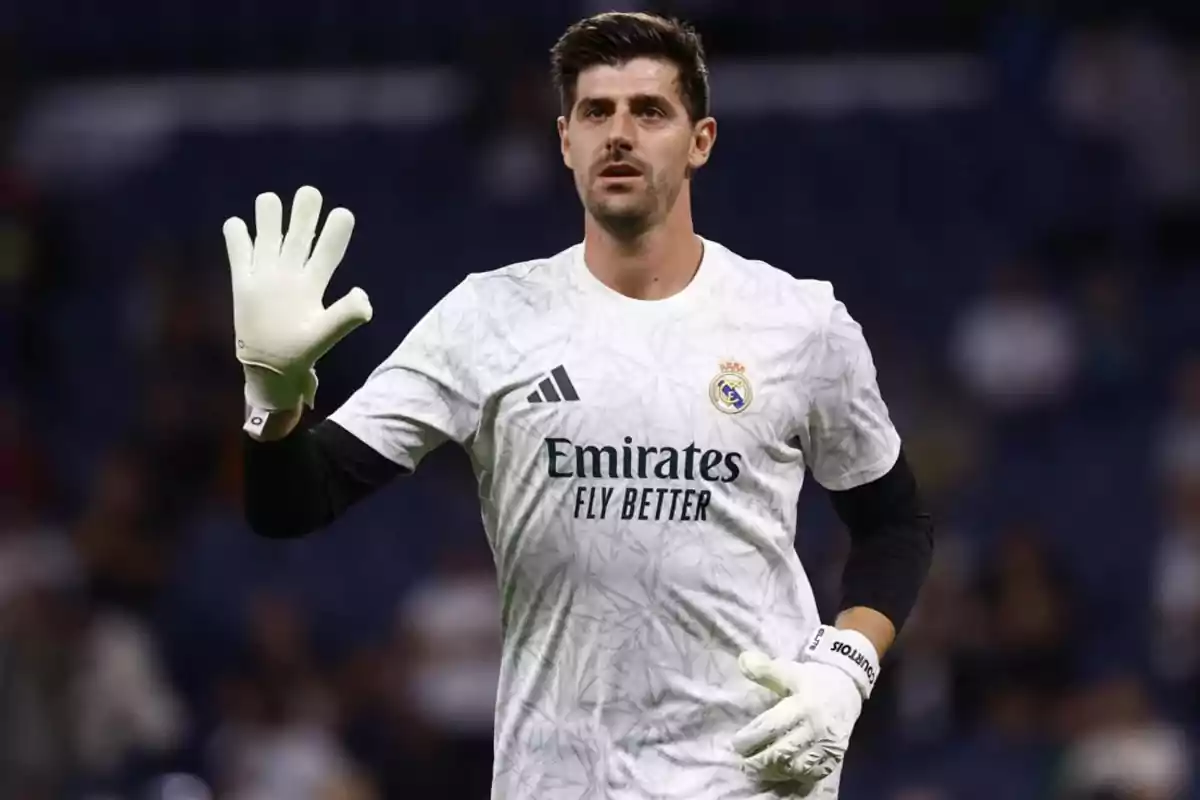 A soccer player in a white uniform and gloves raises his hand on the field. A soccer player in a white uniform and gloves raises his hand on the field.