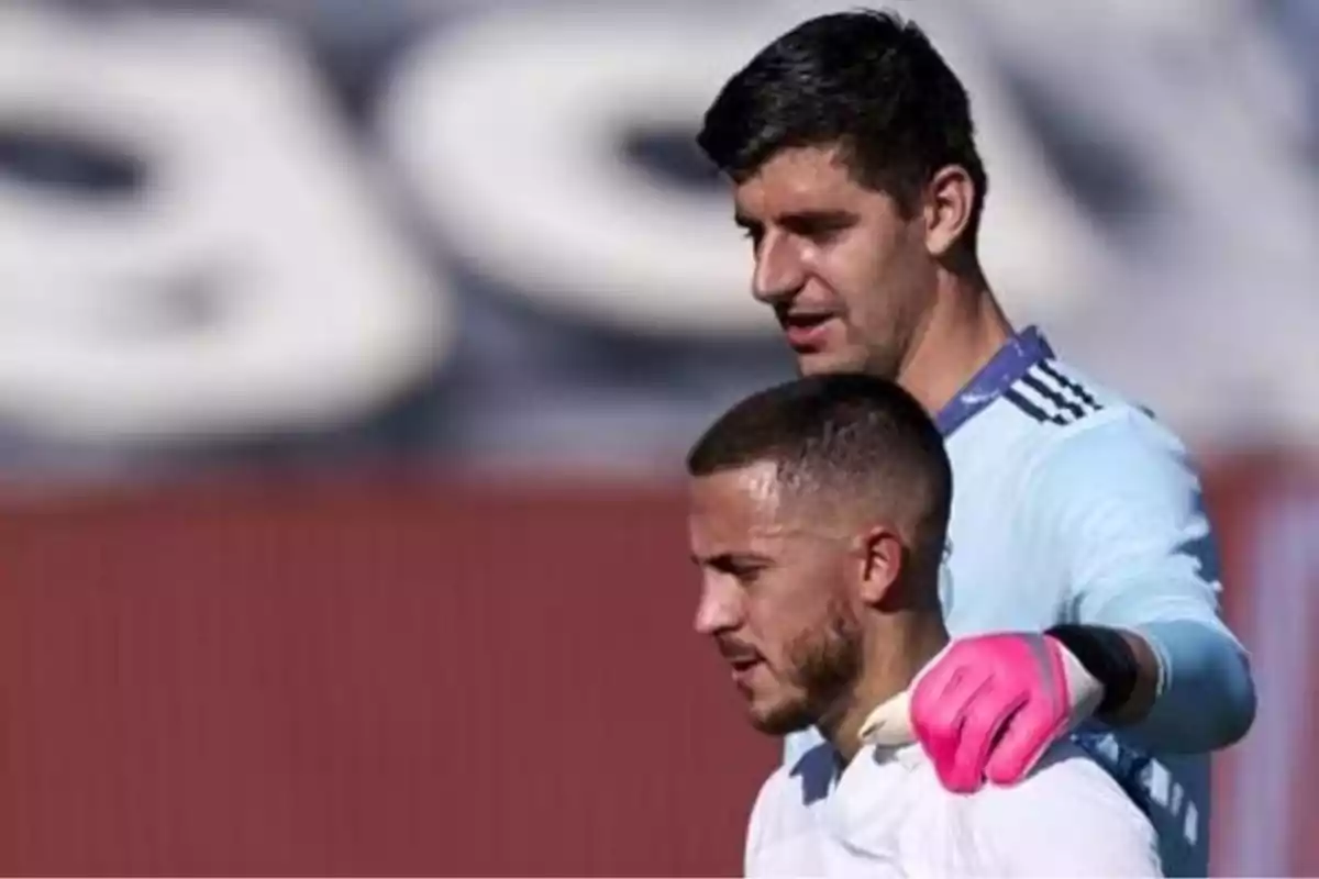 Dos jugadores de fútbol en el campo, uno con guantes rosados y el otro con camiseta blanca.