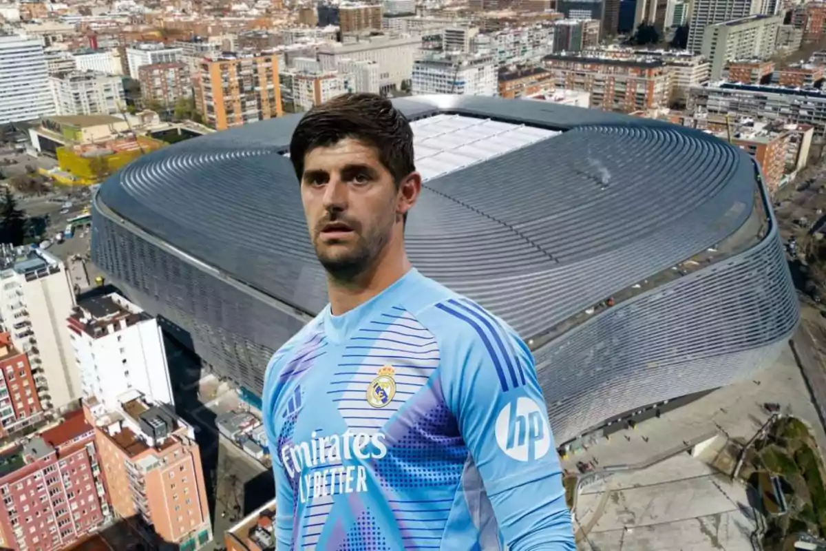 Un jugador de fútbol con uniforme azul claro del Real Madrid frente a un estadio moderno en una ciudad.