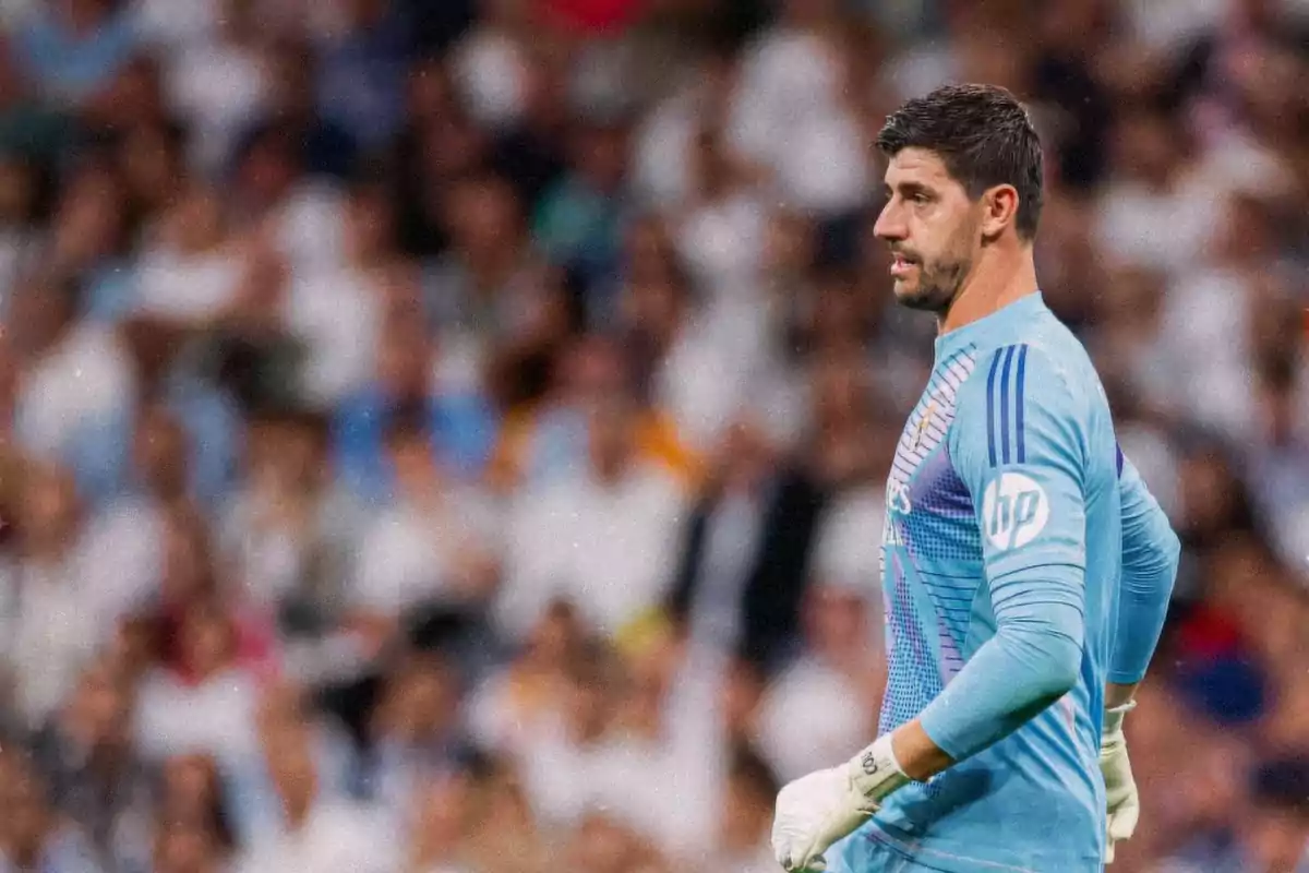 A soccer player in a light blue goalkeeper uniform stands on the field during a match, with the crowd out of focus in the background.