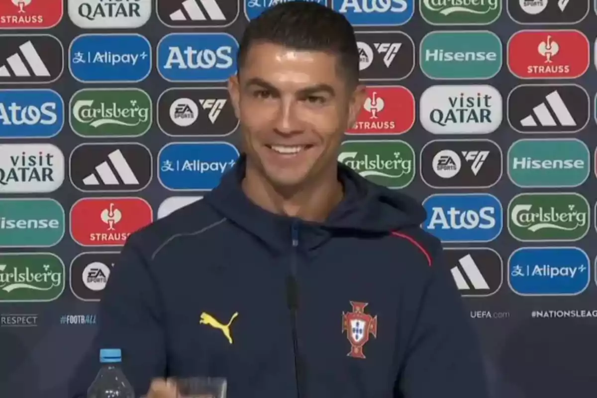 Soccer player wearing a Portugal jacket smiling during a press conference with a sponsors' backdrop Soccer player wearing a Portugal jacket smiling during a press conference with a sponsors' backdrop
