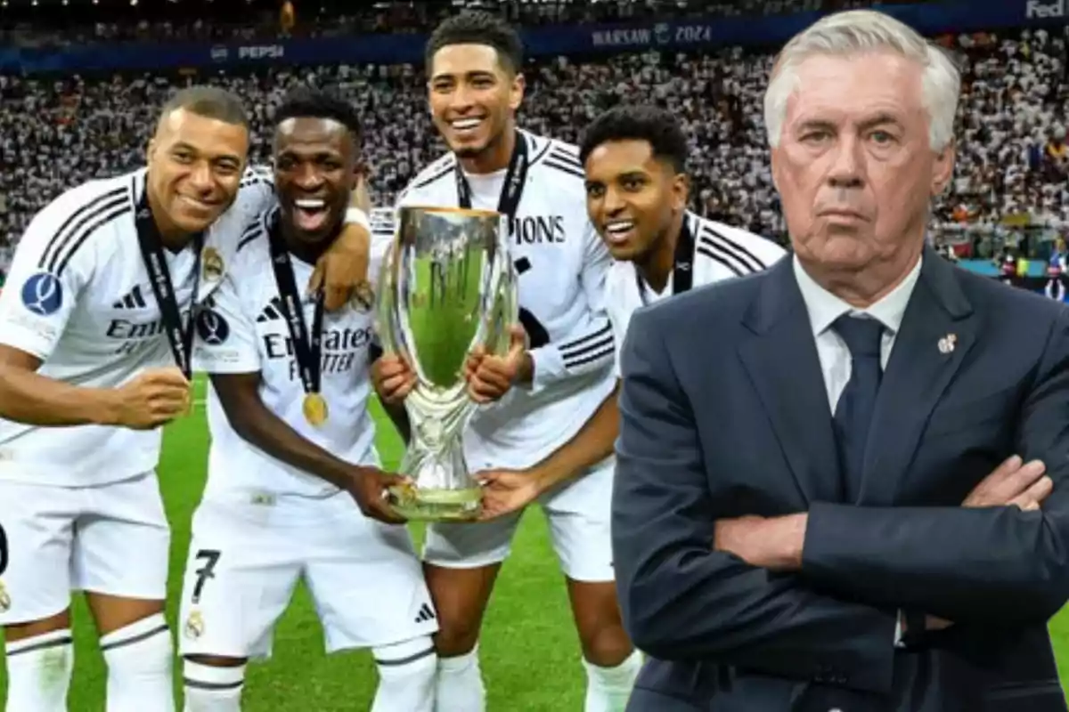 A group of players in white uniforms celebrate with a trophy on the field while a man in a suit watches them with crossed arms.