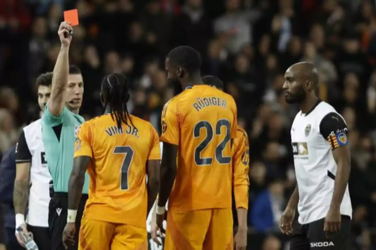 Un árbitro muestra una tarjeta roja a un jugador durante un partido de fútbol, mientras otros jugadores observan la situación.