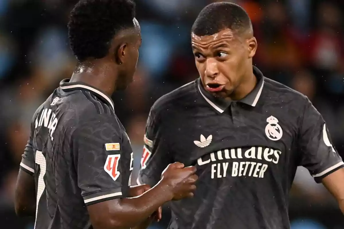 Dos jugadores de fútbol con uniformes oscuros del Real Madrid conversan en el campo durante un partido.