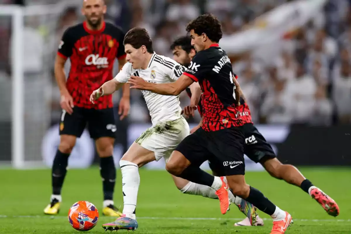 Soccer players compete for the ball in a match, one in a white uniform and the other in a black and red uniform.