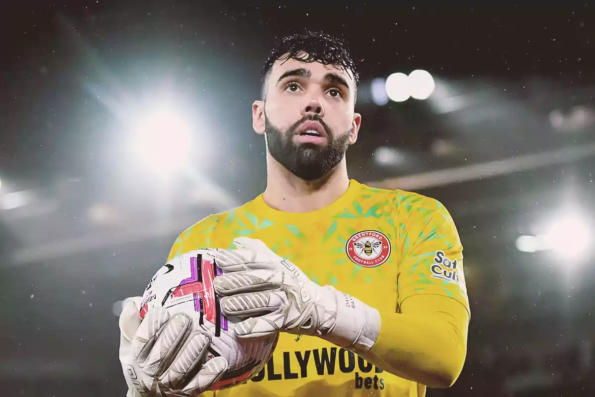 Portero de fútbol con uniforme amarillo sosteniendo un balón durante un partido bajo luces brillantes Portero de fútbol con uniforme amarillo sosteniendo un balón durante un partido bajo luces brillantes
