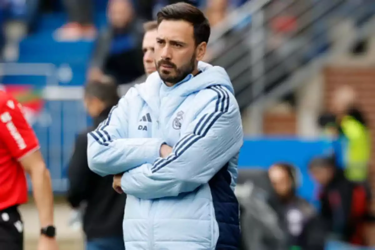 A man in a light blue sports jacket with crossed arms in a sports setting. A man in a light blue sports jacket with crossed arms in a sports setting.