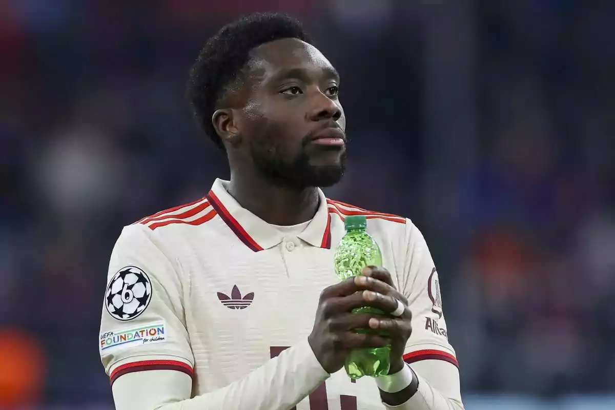 Un jugador de fútbol con uniforme blanco y rojo sostiene una botella verde en sus manos.