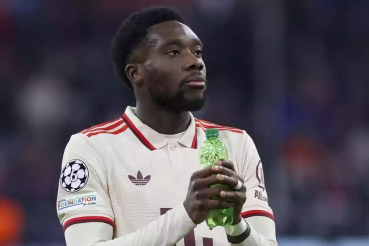 A soccer player in a white and red uniform holds a green bottle in his hands during a match.