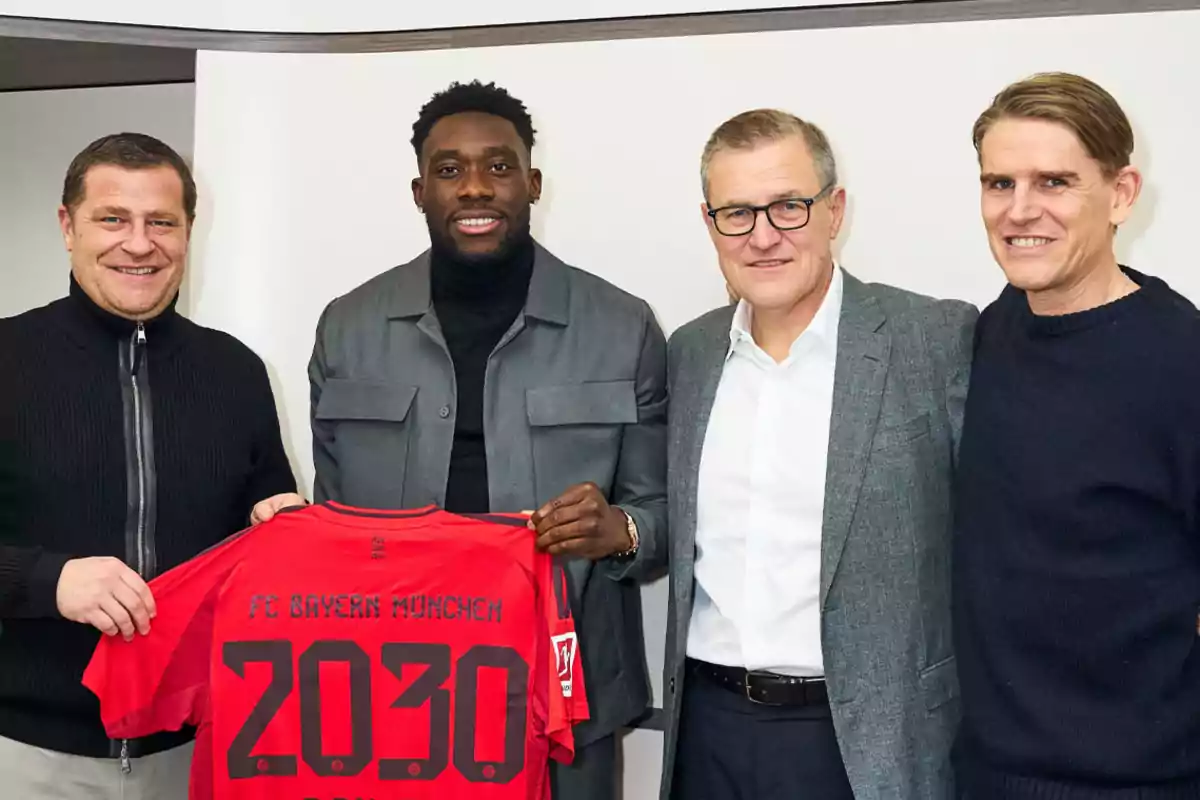 Four people pose together while one of them holds a red FC Bayern Munich jersey with the number 2030.