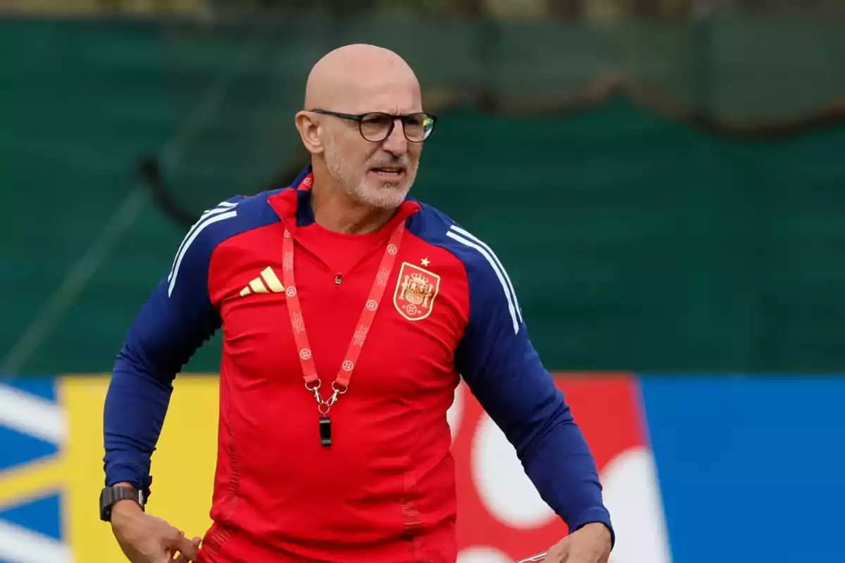 Entrenador de fútbol con gafas y silbato vistiendo uniforme rojo y azul de la selección de España durante un entrenamiento en campo deportivo Entrenador de fútbol con gafas y silbato vistiendo uniforme rojo y azul de la selección de España durante un entrenamiento en campo deportivo