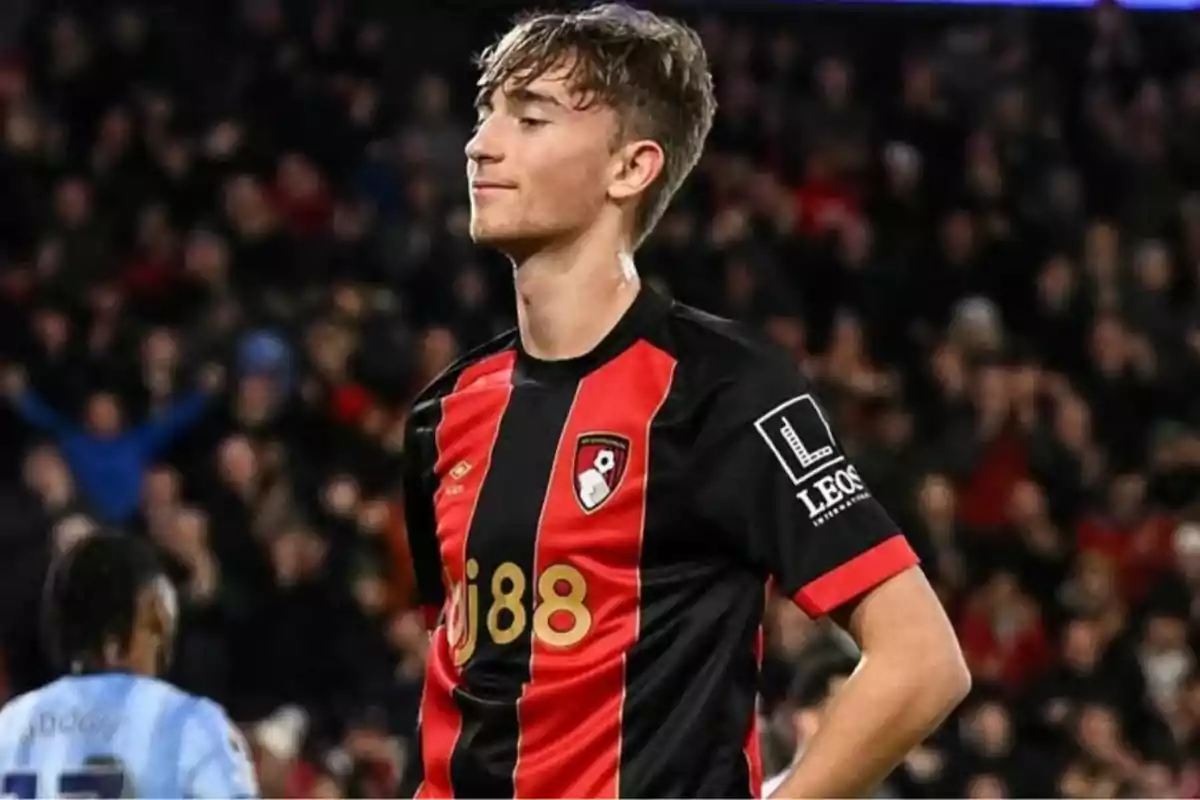 A soccer player in a red and black uniform in a stadium full of spectators. A soccer player in a red and black uniform in a stadium full of spectators.