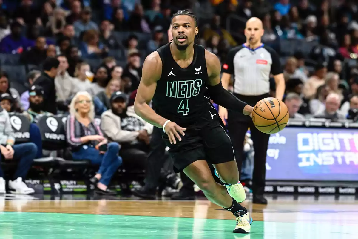 Nets basketball player dribbles the ball during a game with the crowd and a referee in the background. Nets basketball player dribbles the ball during a game with the crowd and a referee in the background.