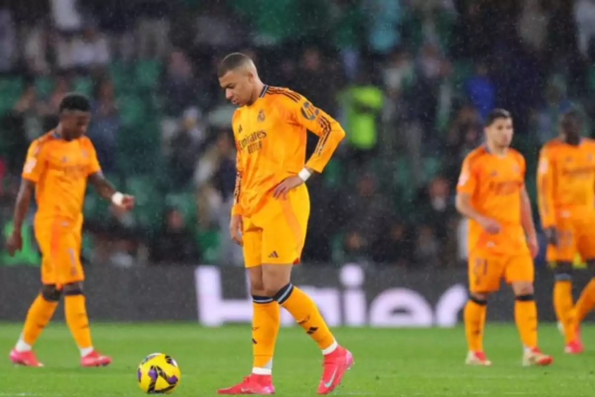 Soccer players in orange uniforms on the field in the rain.