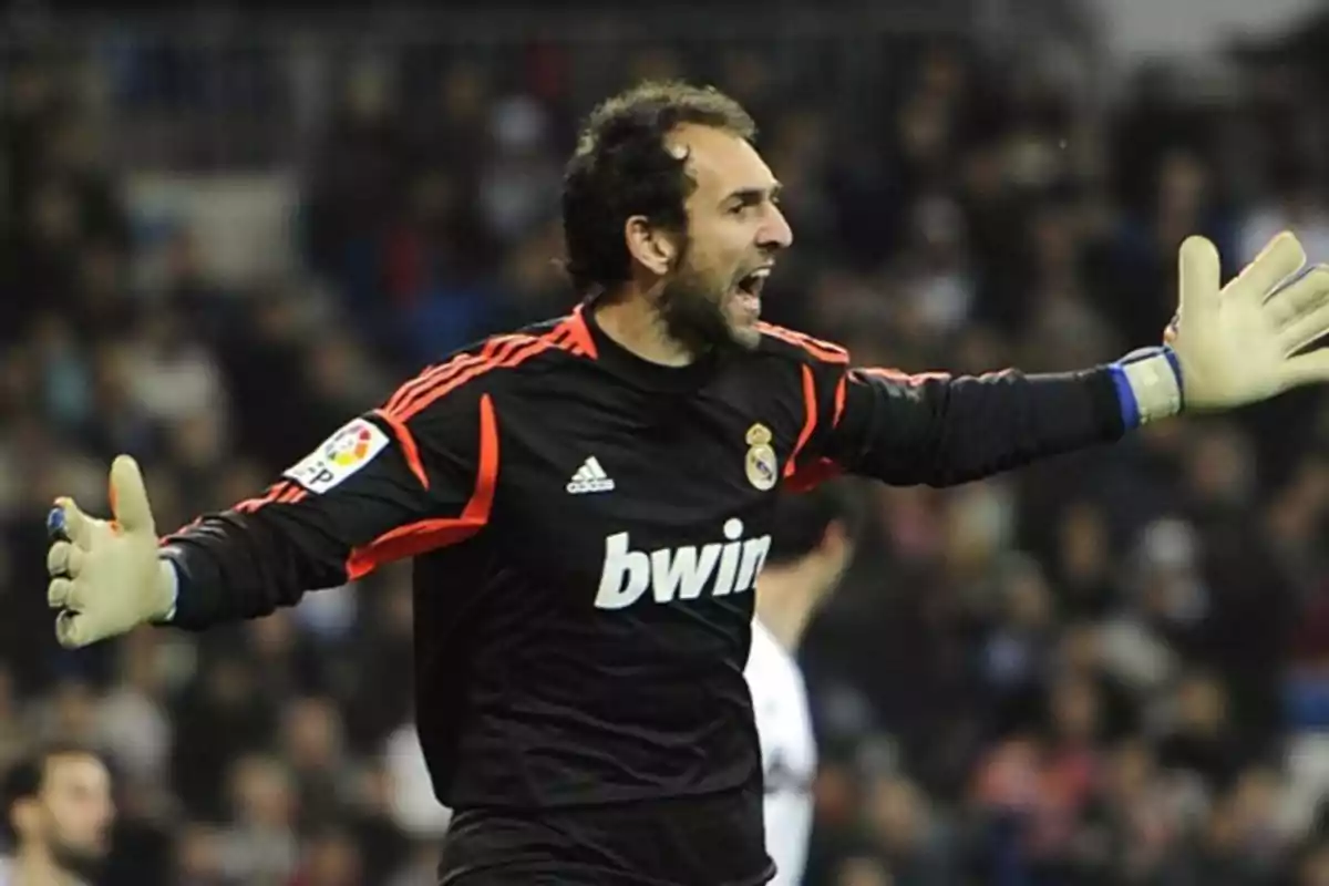 A soccer goalkeeper in a black uniform with orange details gesturing on the field. A soccer goalkeeper in a black uniform with orange details gesturing on the field.