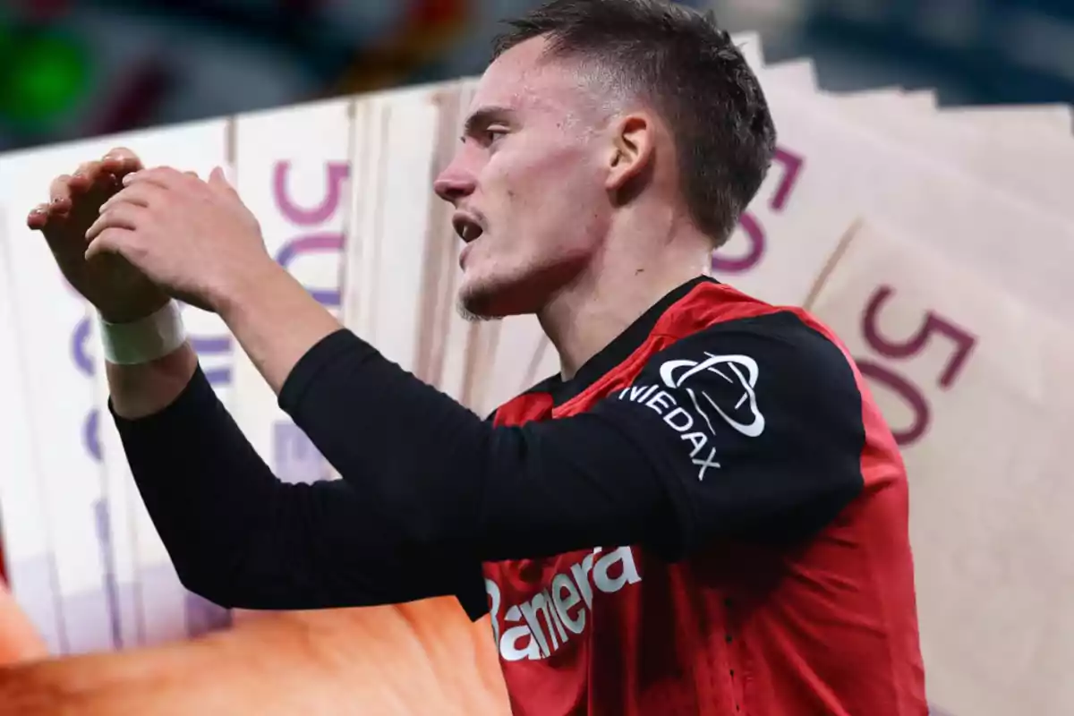 Un jugador de fútbol con uniforme rojo y negro gesticula con las manos frente a un fondo de billetes de 50 euros.