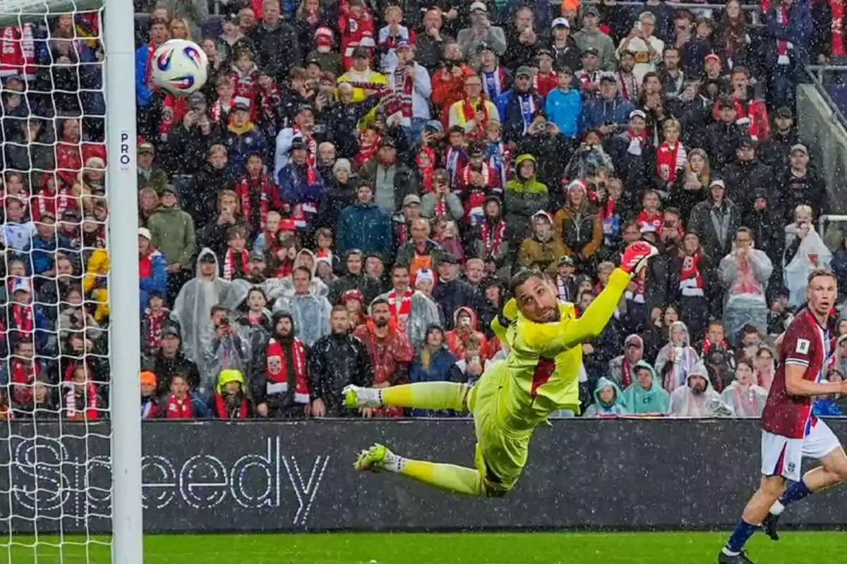 Goalkeeper diving through the air in the rain as a ball goes into the net during a soccer match with a crowd in the background Goalkeeper diving through the air in the rain as a ball goes into the net during a soccer match with a crowd in the background