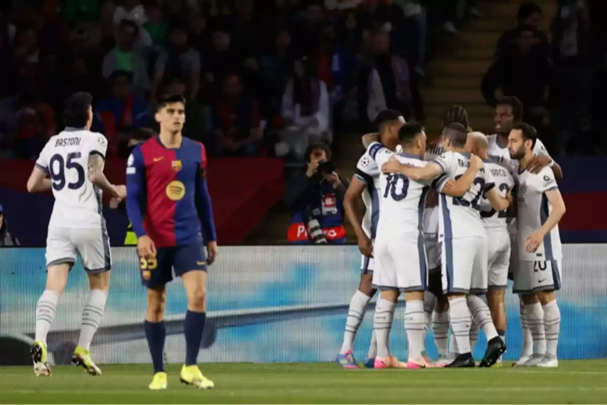 Players from a soccer team celebrate in a group while a player from the opposing team walks nearby. Players from a soccer team celebrate in a group while a player from the opposing team walks nearby.