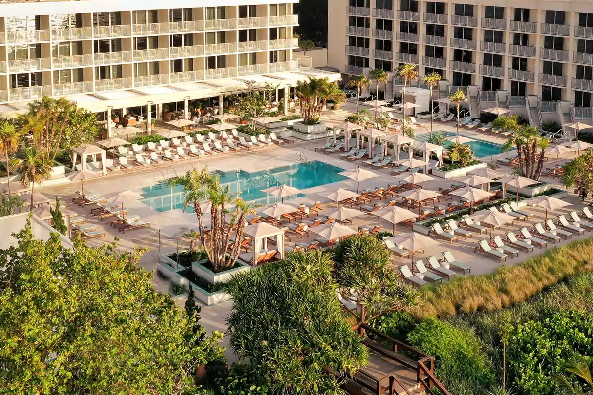 Vista aérea de un lujoso hotel con piscina rodeada de camastros, sombrillas y palmeras