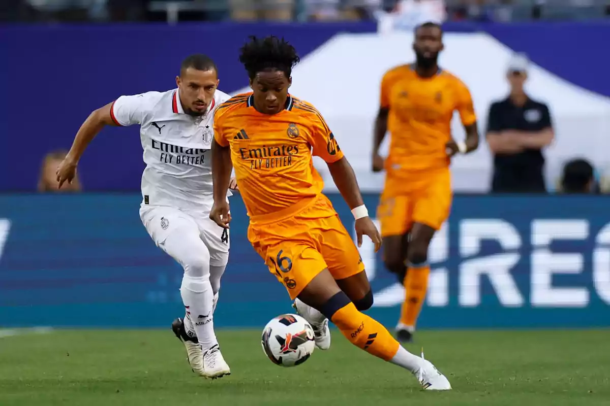 Two soccer players compete for the ball in a match, one wearing white and the other wearing orange. Two soccer players compete for the ball in a match, one wearing white and the other wearing orange.