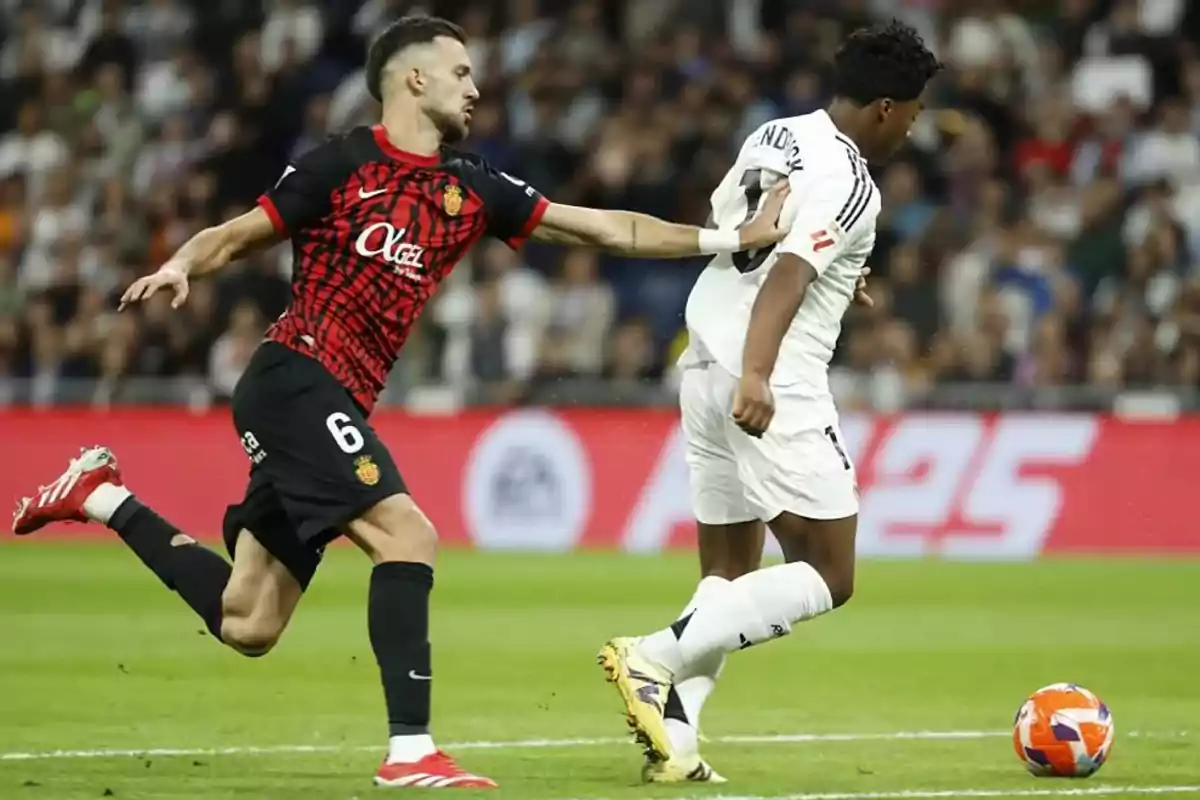 A player in a red and black uniform tries to stop another player in a white uniform during a match. A player in a red and black uniform tries to stop another player in a white uniform during a match.