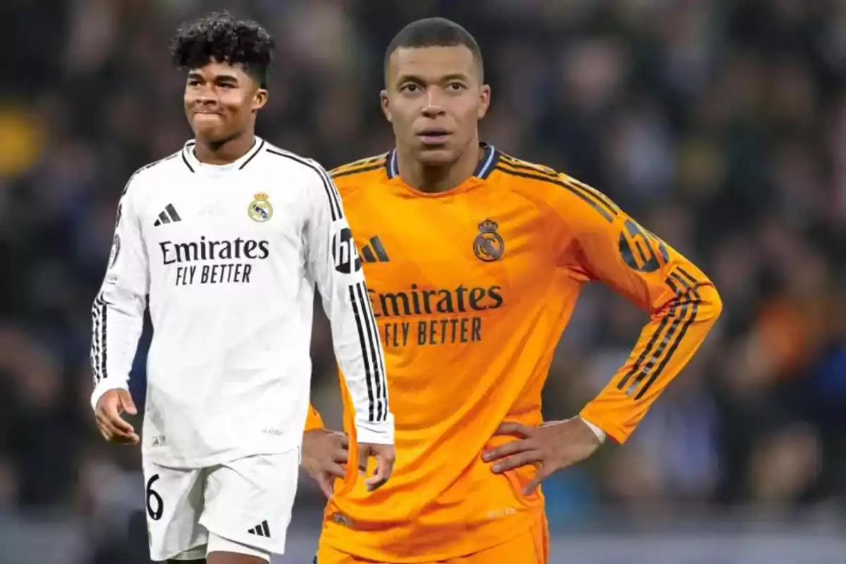 Two players in Real Madrid uniforms, one in a white jersey and the other in an orange jersey, on a soccer field.